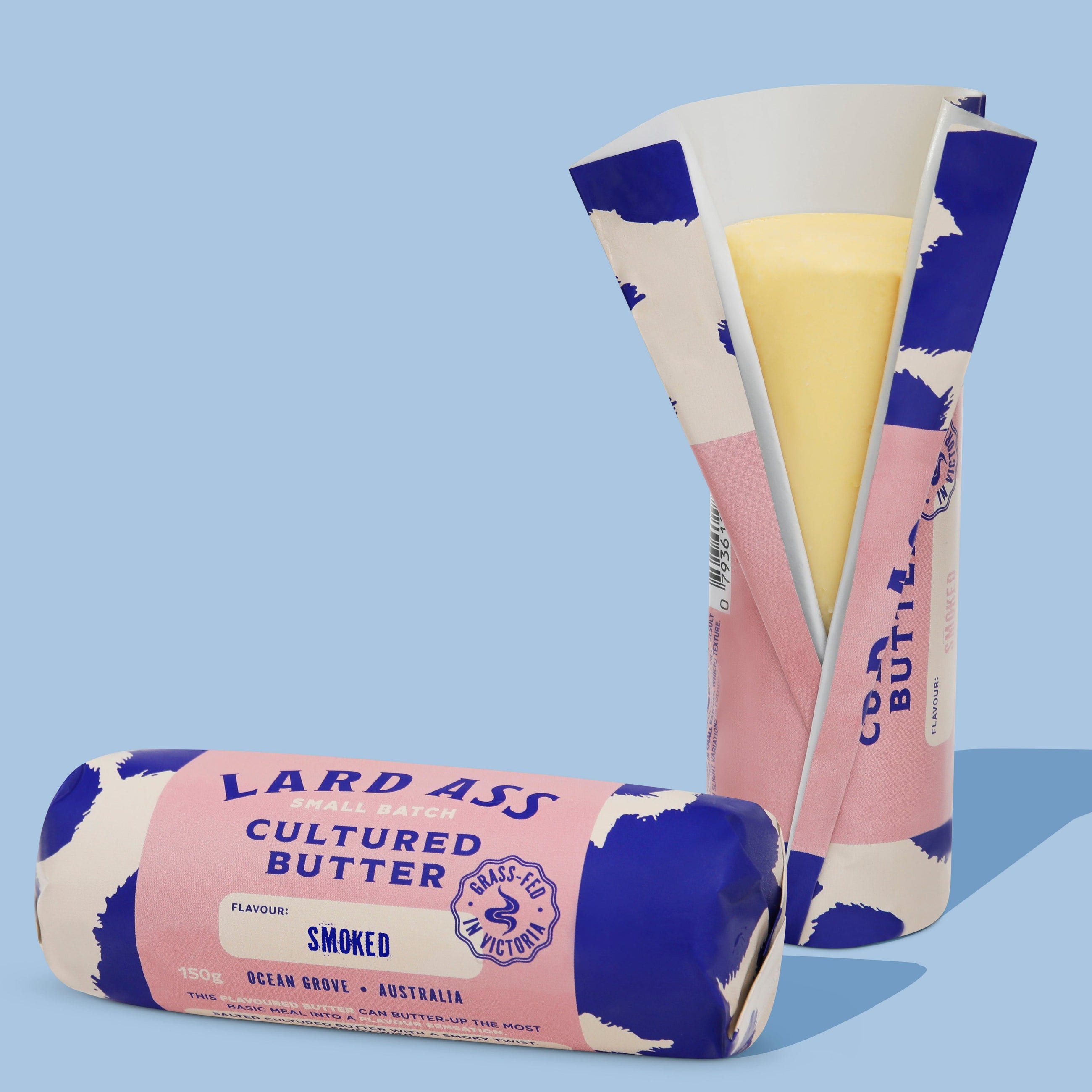 Two wrapped sticks of Lardass Cultured Butter, one standing upright and one lying down, showing the smoked flavor on a light blue background.