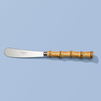A Sabre Paris spreader knife with a silver stainless steel blade and a light brown bamboo handle, shown on a solid light blue background.