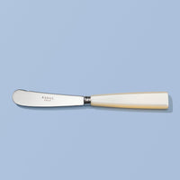 A SABRE Paris butter knife with a silver stainless steel blade and a cream-colored bone handle, displayed horizontally on a solid light blue background.