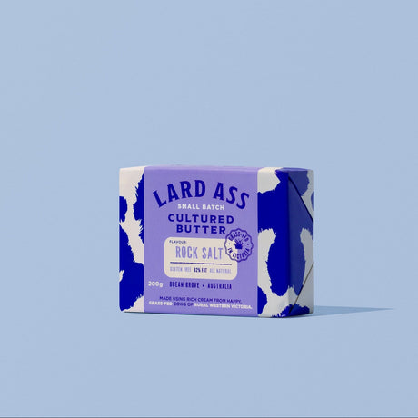 A single bar of Lard Ass Cultured Butter Rock Salt soap standing upright on a light blue background.