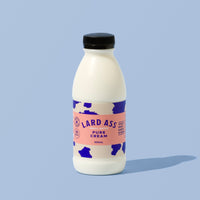 A 300ml bottle of Lard Ass Pure Cream against a solid light blue background. The bottle is white with a black cap and a pink and blue cow-print label.